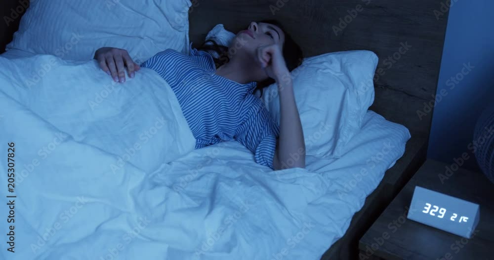Young brunette woman in blue pajama sleeping in the bed at night and moving from side to side. Inside Young brunette woman in blue pajama sleeping in the bed at night and moving from side to side. Inside