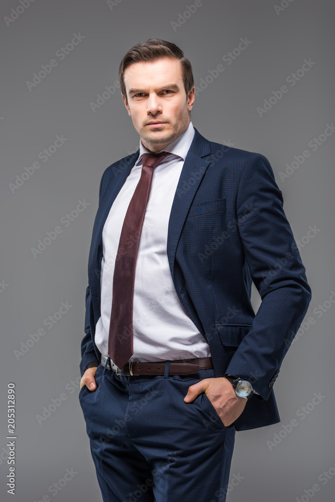 handsome businessman in formal wear with hands in pockets, isolated on grey handsome businessman in formal wear with hands in pockets, isolated on grey