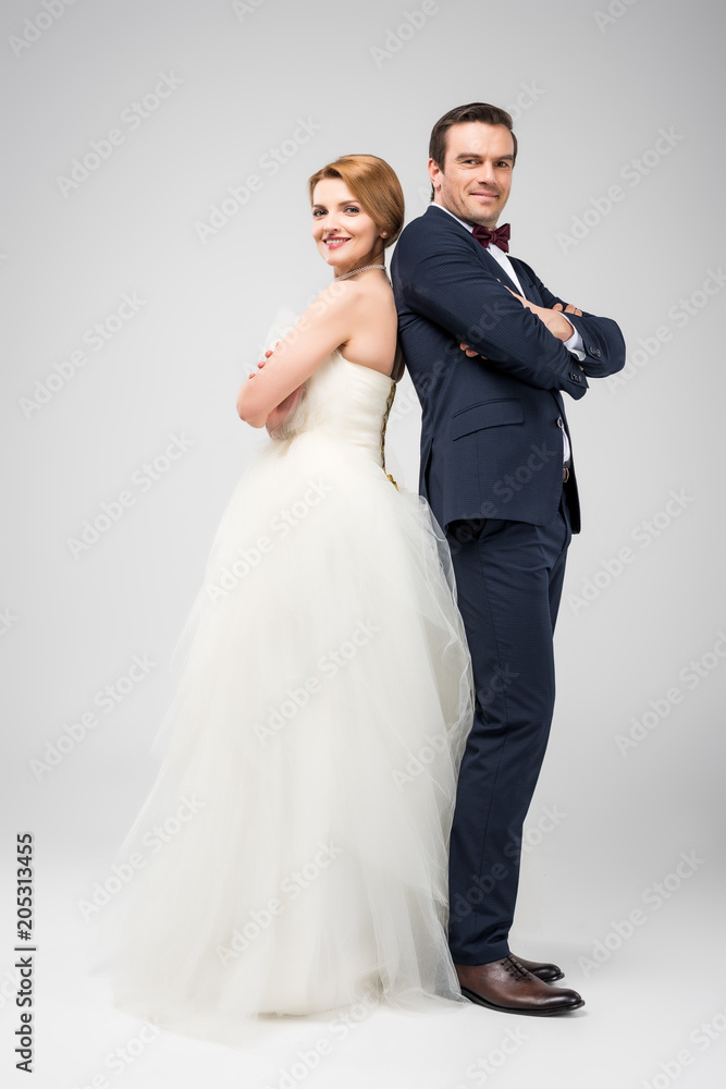 wedding couple standing back to back with crossed arms, isolated on grey