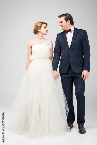 groom in tuxedo and bride in wedding dress holding hands  isolated on grey