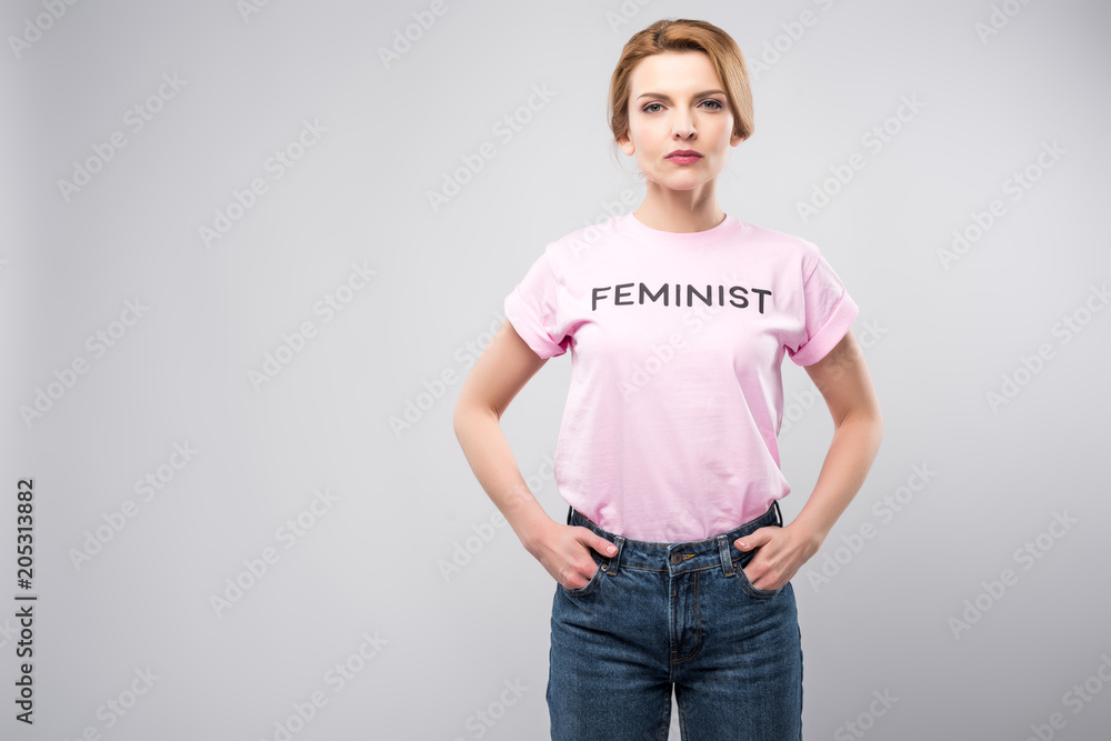 woman in pink feminist t-shirt posing with hands in pockets, isolated on grey woman in pink feminist t-shirt posing with hands in pockets, isolated on grey