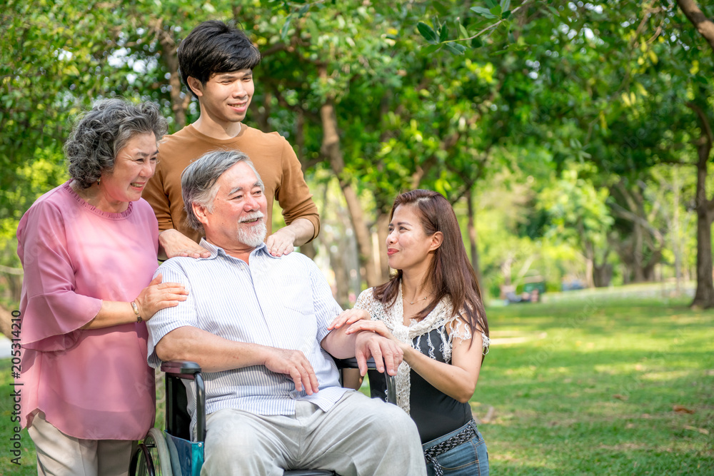 Senior man with his family in park. Chinese old man in wheel chair and his senior chinese wife, grand son and daughter relaxing together, talking to each other. Family insurance concept.