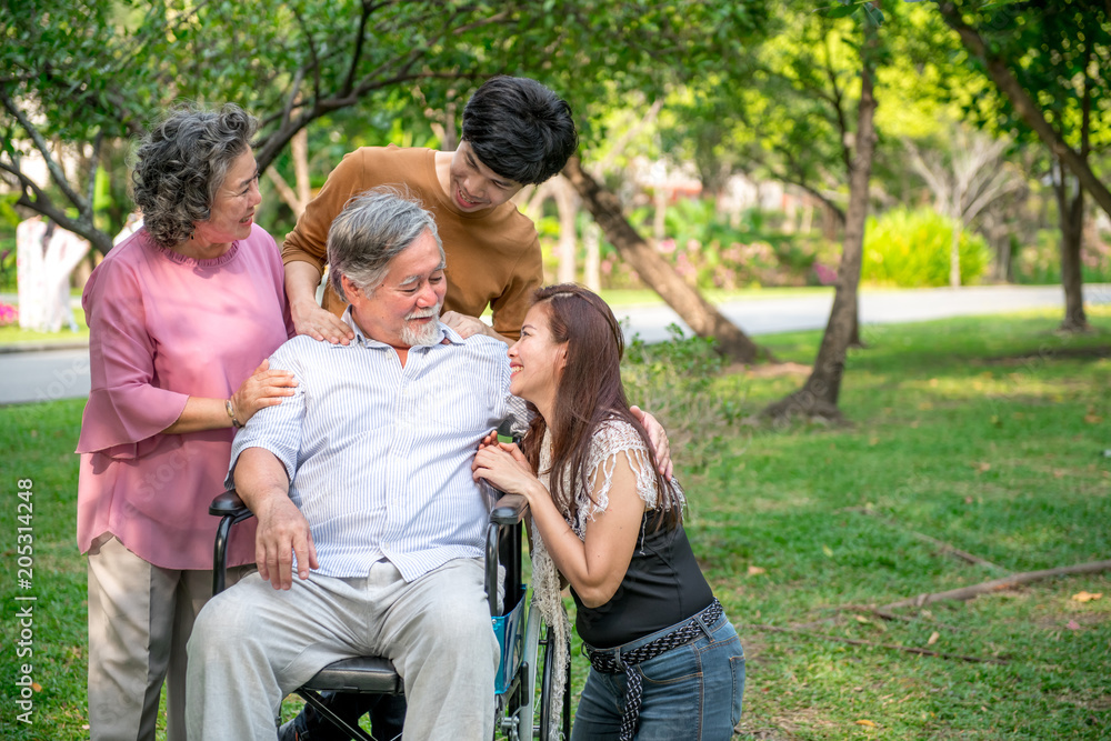 Senior man with his family in park. Chinese old man in wheel chair and his senior chinese wife, grand son and daughter relaxing together, talking to each other. Family insurance concept. Senior man with his family in park. Chinese old man in wheel chair and his senior chinese wife, grand son and daughter relaxing together, talking to each other. Family insurance concept.