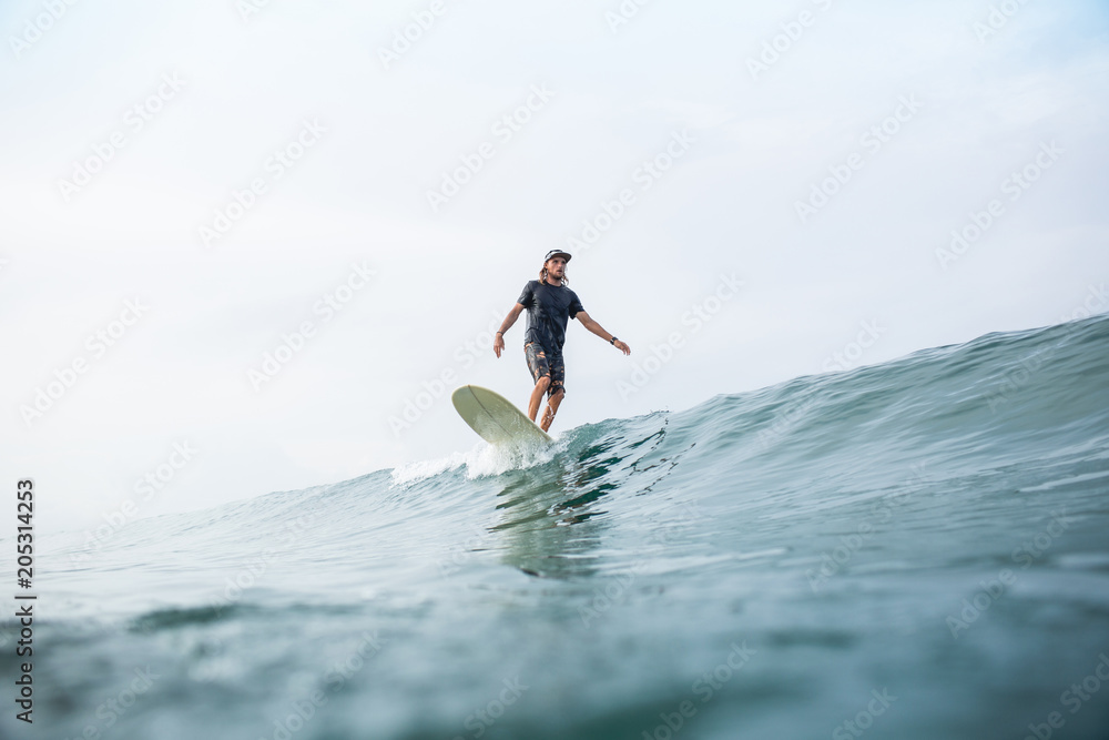 young athletic man riding surfboard in ocean during summer vacation