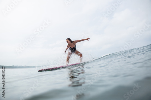 side view of sportive young woman in black swimsuit riding on surfboard in ocean