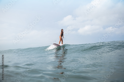 attractive young woman standing on surfboard in ocean