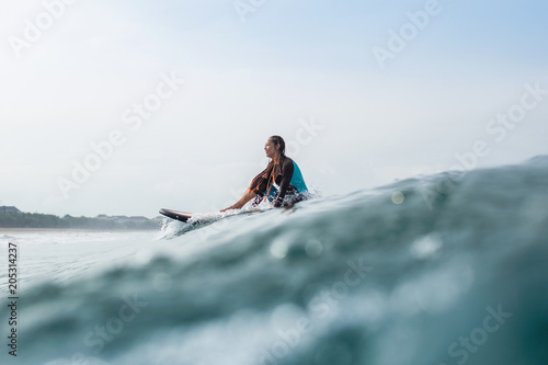 beautiful young woman sitting on surfboard in ocean