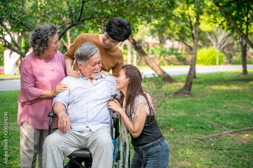 Senior man with his family in park. Chinese old man in wheel chair and his senior chinese wife, grand son and daughter relaxing together, talking to each other. Family insurance concept.