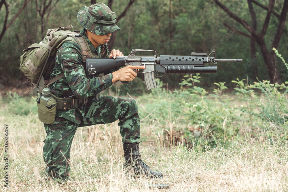 Fototapeta premium Soldier reloading his assault rifle. Chinese professional soldier reloading his weapon and putting his magzine inside his gun. Kneeing down action.