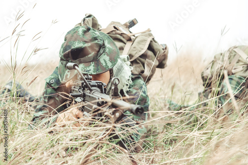 Soldier hiding in bushes ready to shoot. Ambush his ememy, ready his assault rifle. Hiding below the tree line. Military combat training concept. © Baan Taksin Studio