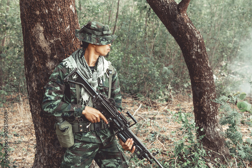 Soldier standing behind a tree ready to attack. Chinese male soldier standing behind a large tree looking around for his ememy.
