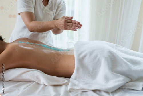 Hand of masseuse sprinkle salt down at back while young asian woman relaxing in the spa having salt scrub massage. healthy lifestyle and relaxation concept.