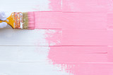 Close up woman hand holding brush painting pink color on a white wooden table