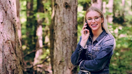 Young Cheerful Blond Woman Talking On Phone While Standing In Forest