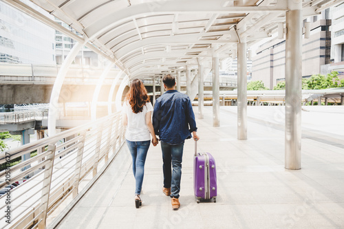 A handsome boyfriend or traveler man hold his girlfriend’s hand and walk together. They love journey at foreign country. They love jeans fashion. Guy drag suitcase. They have enjoy the trip with space