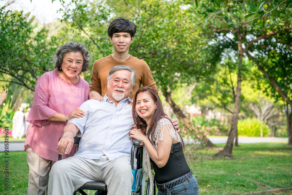 Senior man with his family in park. Chinese old man in wheel chair and his senior chinese wife, grand son and daughter relaxing together, talking to each other. Family insurance concept.