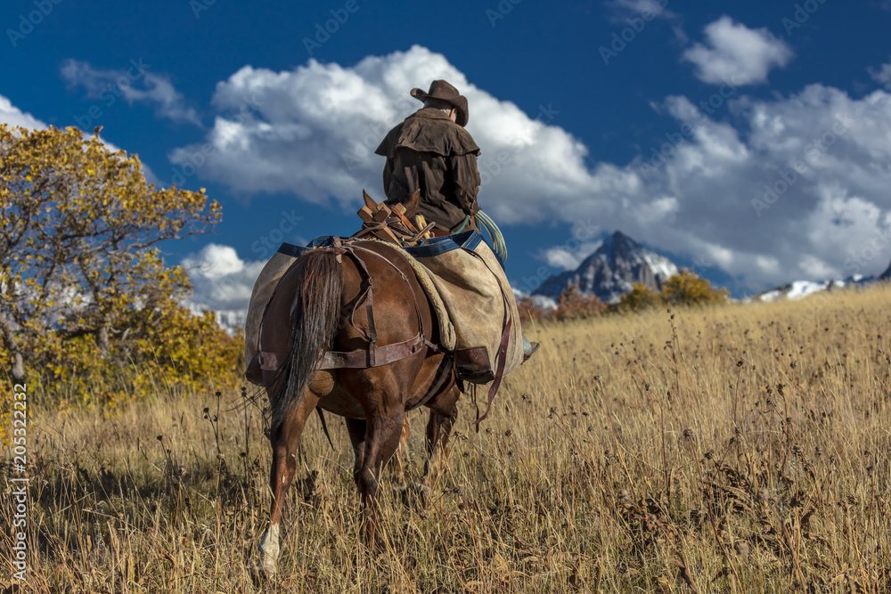 Older Cowboy leads packhorse across historic Last Dollar Ranch on Hastings Mesa, SW Colorado, San Juan Mountains