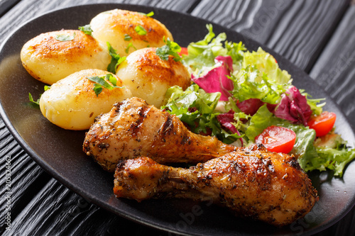 Serving of grilled chicken legs with potatoes and fresh salad closeup on a plate. horizontal
