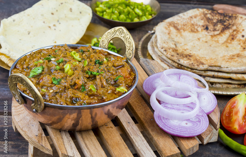 Indian Cuisine Sev Tamatar Also Called Sev Tamaeta or Sev Tameta is Served With Chapati, Papad, Onion or Raita. It is Made With Tomato And Onion Gravy With a Twist of Spicy Sev on Wooden Table photo
