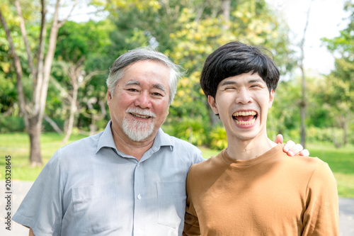 Father and son in park portrait. Retired chinese father with his son holding each other, happy and smiling. Successful family love and relationship concept.