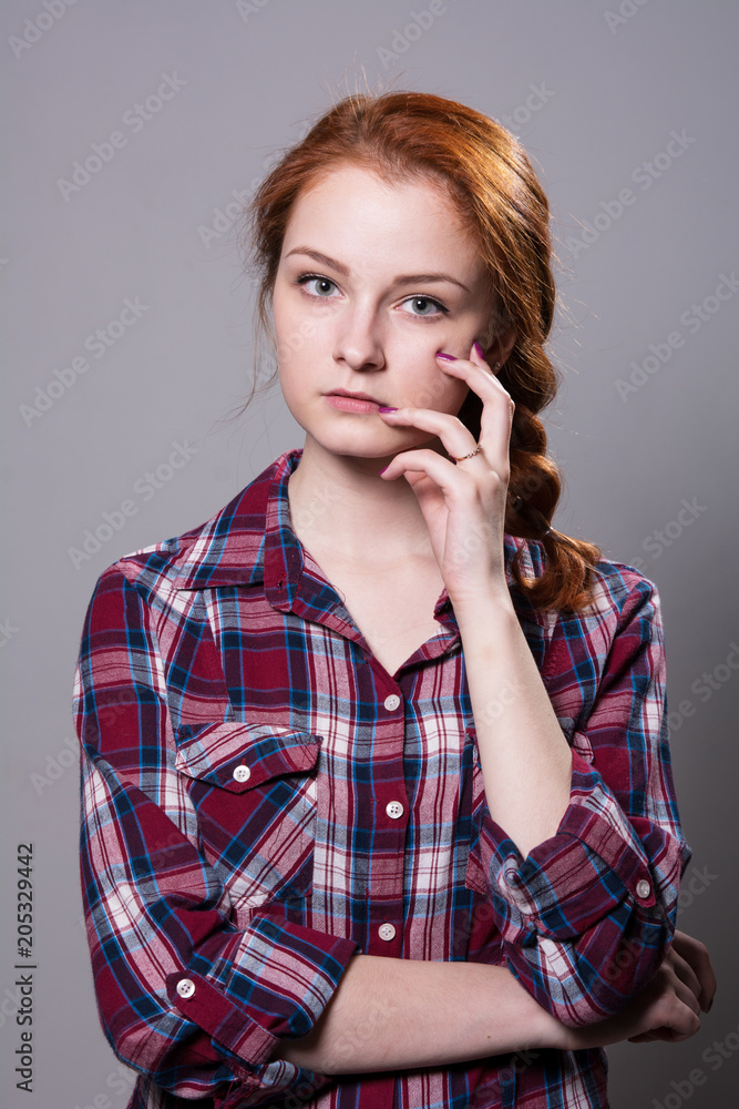 Young red-haired girl in a plaid shirt with fingers on his cheek Young red-haired girl in a plaid shirt with fingers on his cheek