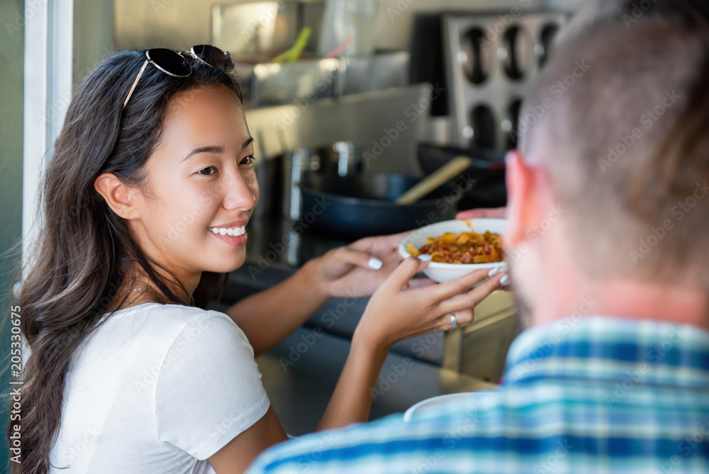 Happy young Asian woman getting pasta from food truck Happy young Asian woman getting pasta from food truck
