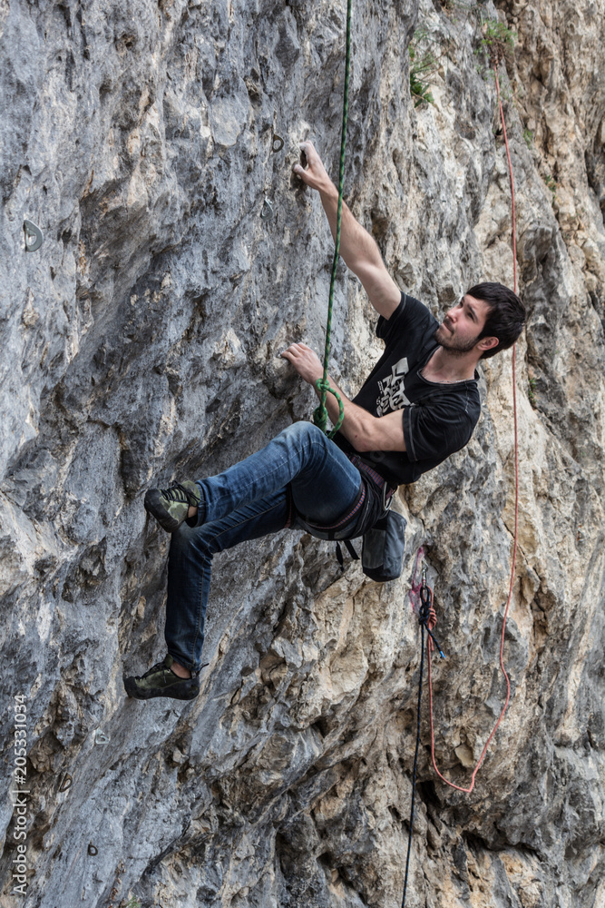 A climber in climbing gear scrambles up the rock