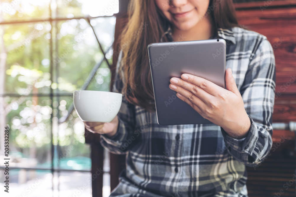Closeup image of a woman holding and using tablet pc while drinking coffee in cafe Closeup image of a woman holding and using tablet pc while drinking coffee in cafe