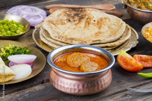 Indian Traditional Cuisine Gatta Curry Also Called Gatte ki Sabji or Besan Gatta is a Rajasthan Famous Food Served with Chapati, Onion, Raita or Papad on Wooden Background