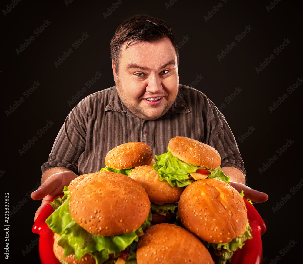 Fat man eating fast food hamberger and carries treat for friends on tray. Breakfast for overweight person. Comfortable clothes for work. Fatso with tray of harmful food. Mass obesity due to poor foods
