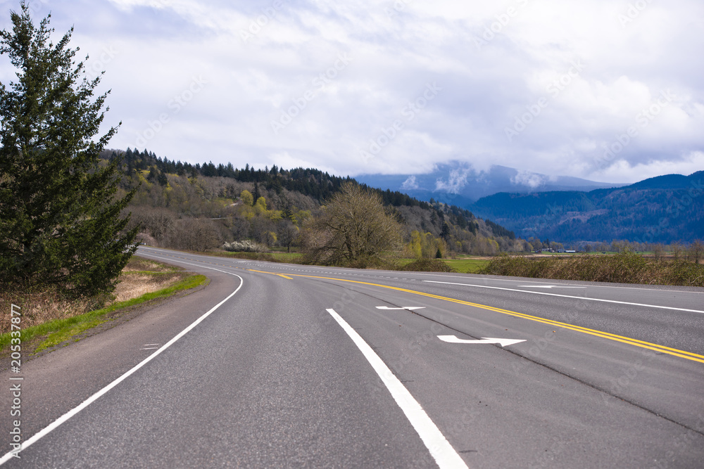Wide multi-lane road with markings passes through picturesque Columbia Gorge area with meadow forest and mountain Wide multi-lane road with markings passes through picturesque Columbia Gorge area with meadow forest and mountain
