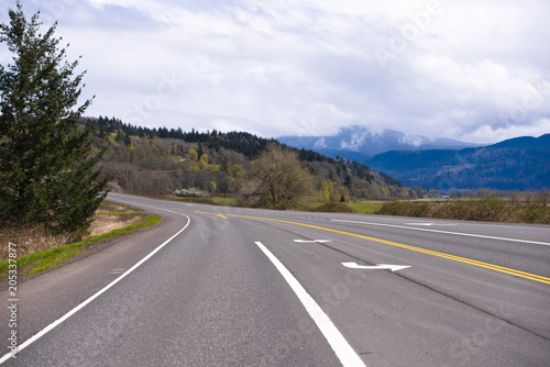 Wide multi-lane road with markings passes through picturesque Columbia Gorge area with meadow forest and mountain © vit