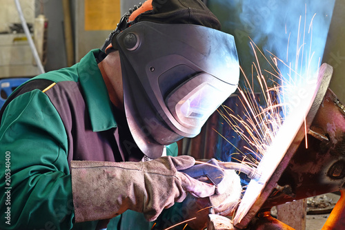 Schweißer am Arbeitsplatz in einer Werkstatt schweißt Metall // Welder at the workplace in a workshop welds metal
