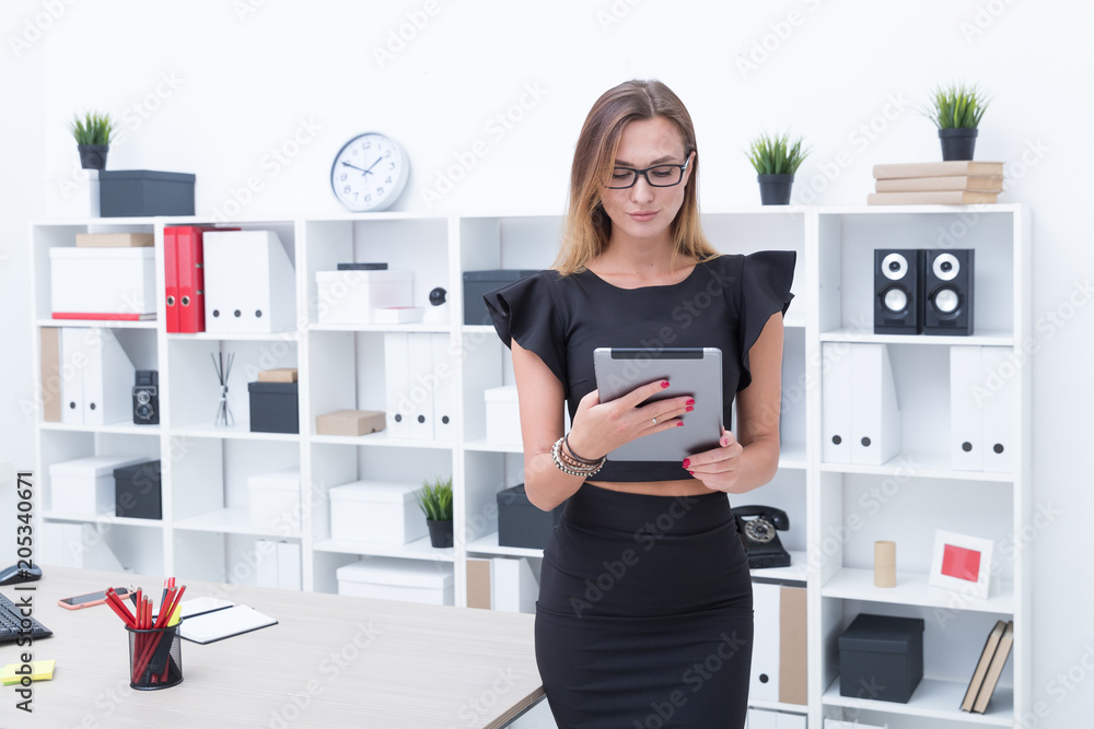 A young manager stands near a table with a tablet in the office A young manager stands near a table with a tablet in the office