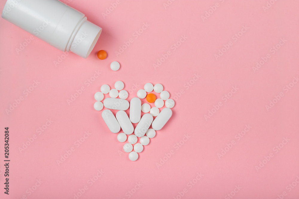 round white pills lined in the shape of a heart poured out on a pink background round white pills lined in the shape of a heart poured out on a pink background