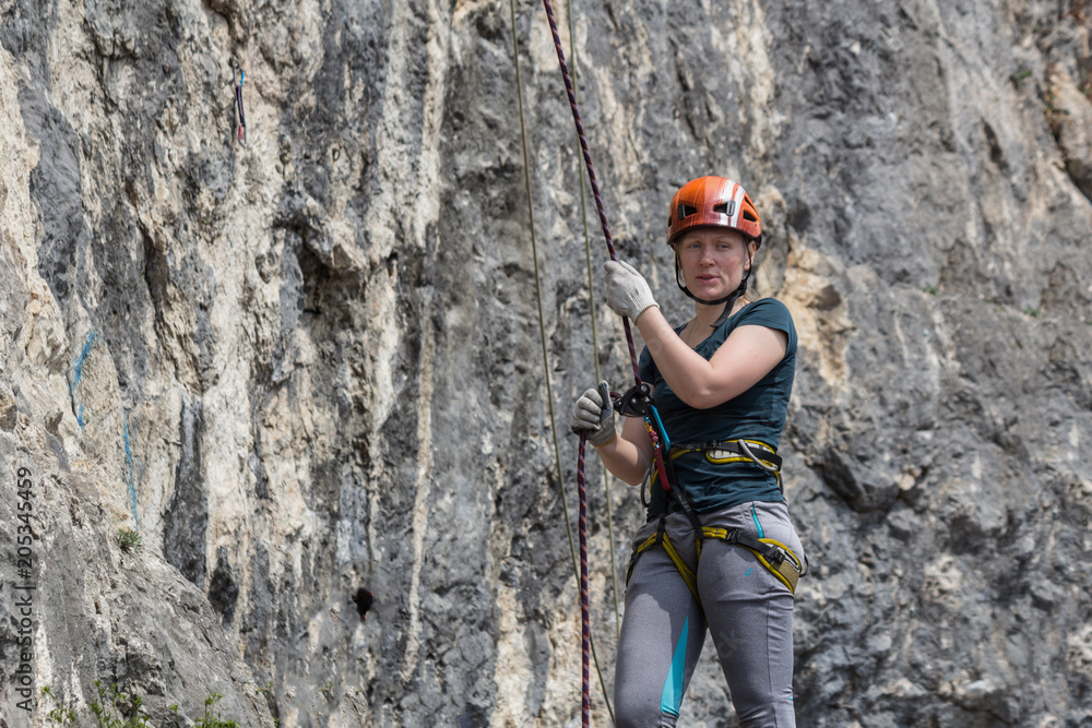 A woman climber in full gear (helmet, safety system etc) is insured by a climber standing near a rock route A woman climber in full gear (helmet, safety system etc) is insured by a climber standing near a rock route