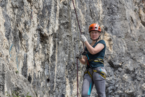 A woman climber in full gear (helmet, safety system etc) is insured by a climber standing near a rock route