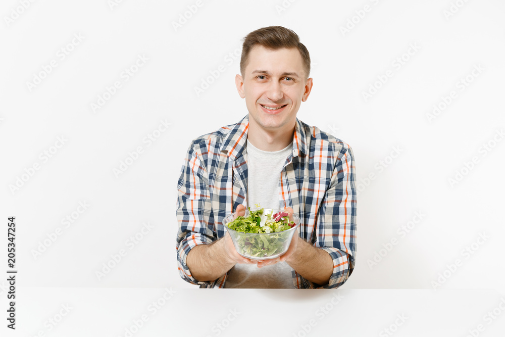 Man sits at table with green detox smoothies, salad in glass bowl, cucumber, burger, fries, cola in glass isolated on white background. Proper nutrition, healthy lifestyle, fast food, choice concept. Man sits at table with green detox smoothies, salad in glass bowl, cucumber, burger, fries, cola in glass isolated on white background. Proper nutrition, healthy lifestyle, fast food, choice concept.