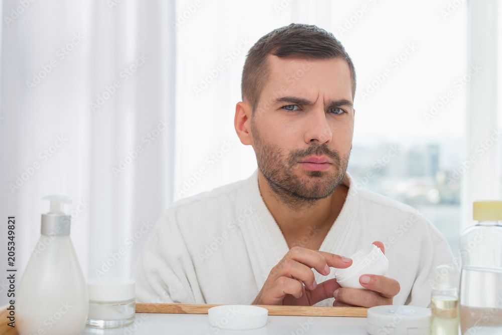 Facial care. Nice pleasant man holding a facial cream while caring about his skin Facial care. Nice pleasant man holding a facial cream while caring about his skin
