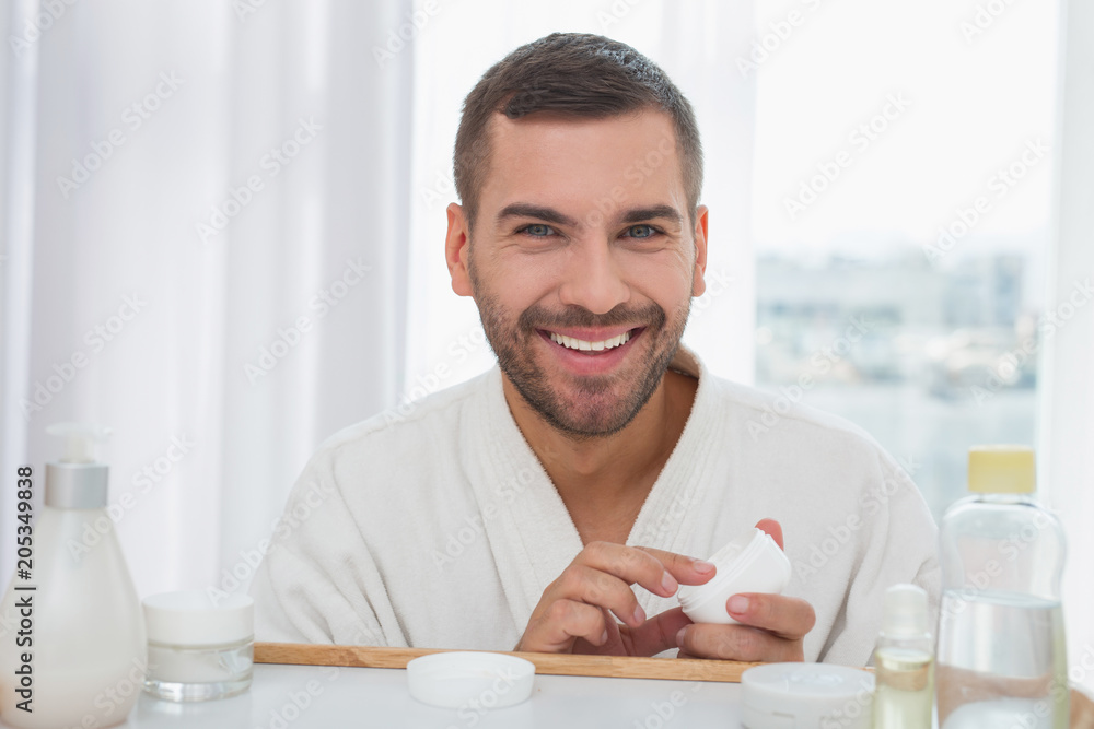 Skin care. Cheerful nice man holding a bottle of cream while caring about his skin Skin care. Cheerful nice man holding a bottle of cream while caring about his skin