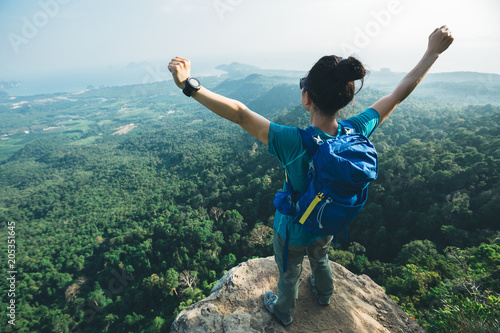 successful woman hiker cheering on mountain peak cliff edge