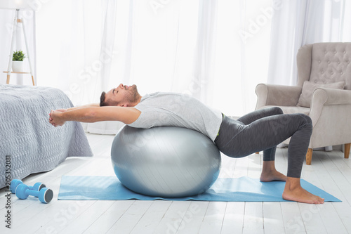 Sport exercises. Nice well built man lying on a med ball while exercising