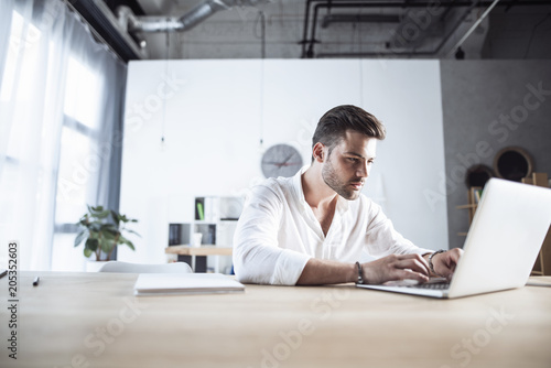 A young man working on his laptop under the clock. Communicate about business, technology, deadlines, focus, concetration, productivity, modern working environments photo