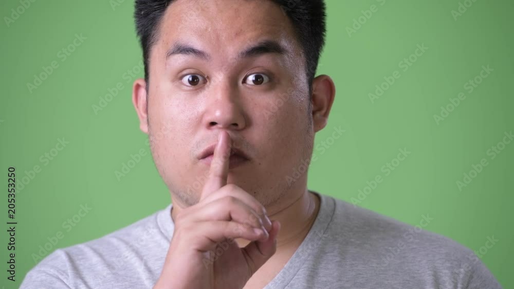 Young handsome overweight Asian man against green background Young handsome overweight Asian man against green background