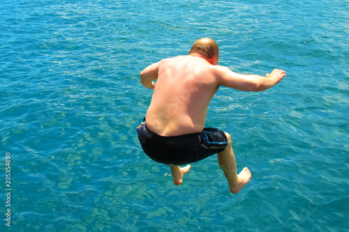a fat man running jump into the deep waters of the tropical sea on a hot sunny day; back view