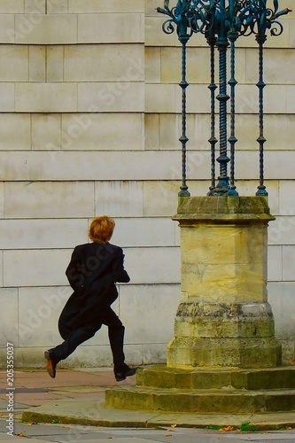 a boy, dressed in a black tailcoat running along the street; young student of Eton College (UK)