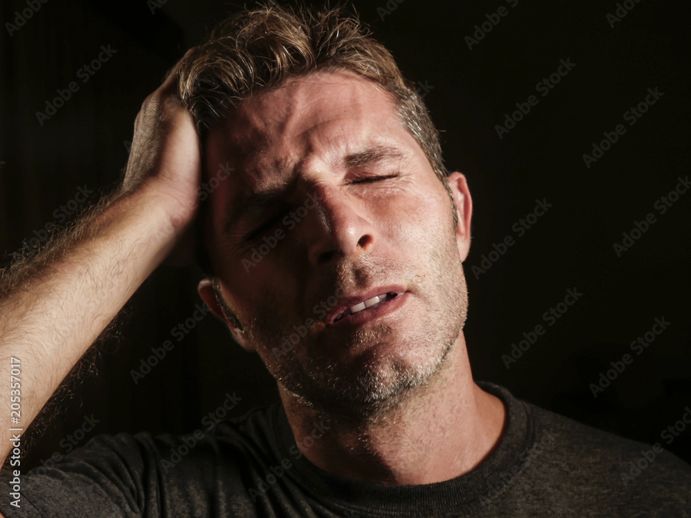 Obraz premium young attractive and sad man suffering depression and headache with hand on his tempo head in stress looking worried and sick isolated on black