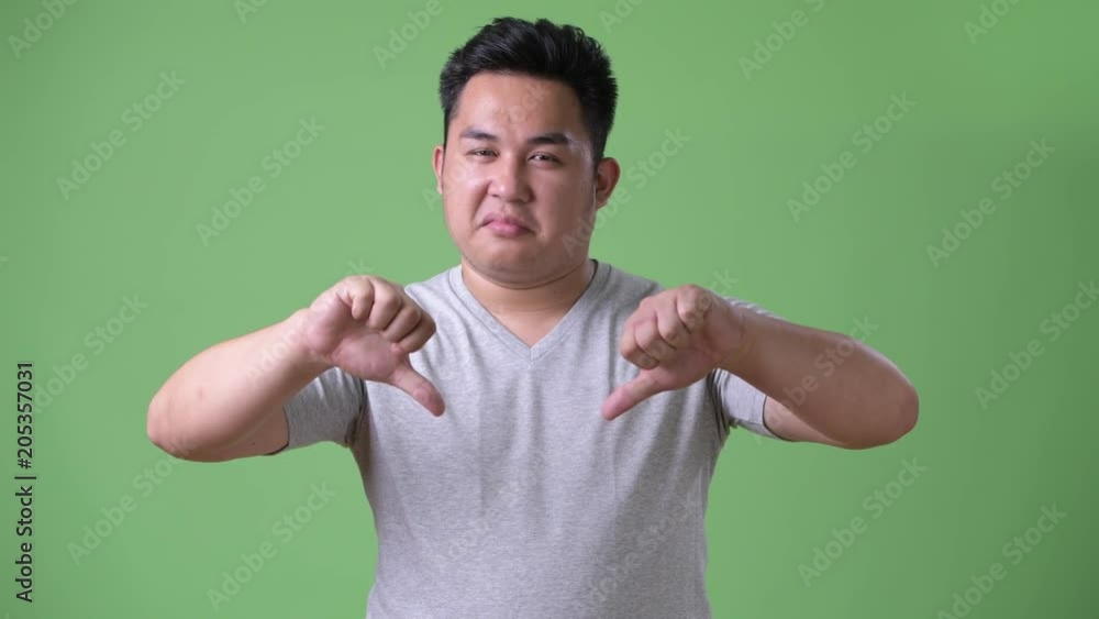 Young handsome overweight Asian man against green background Young handsome overweight Asian man against green background