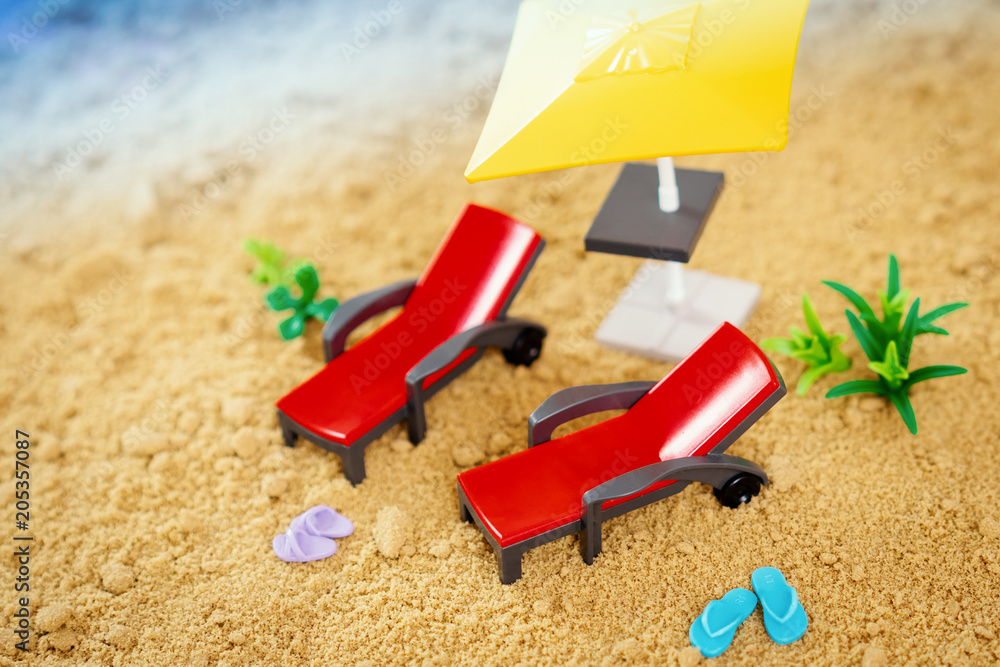 two toy deckchairs and small blue flip-flops on the sand next to the sea in summer