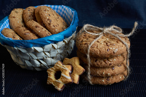 homemade oat cookies with sunflower seeds in and near blue checkered basket on black background